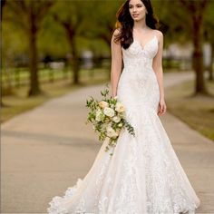 a woman in a wedding dress is standing on the sidewalk holding a bouquet and looking at the camera