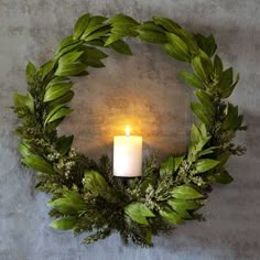 a wreath with a lit candle in the middle and greenery around it on a wall