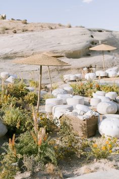 several white vases sitting on the ground near plants and umbrellas in front of some rocks