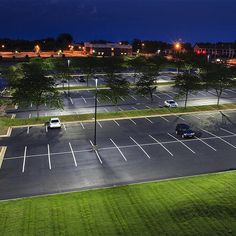 an empty parking lot at night with cars parked in the lot and buildings lit up