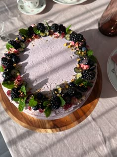 a cake with berries and leaves on it sitting on a wooden platter next to tea cups