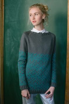 a woman standing in front of a green wall wearing a sweater and white pants with her hands on her hips