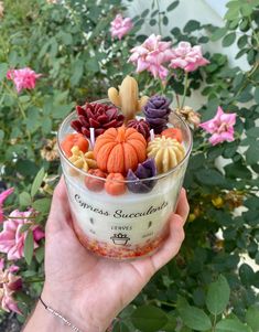 a person holding up a cup filled with candy and candies in front of flowers