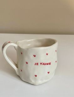 a white ceramic mug with red hearts and the words je t'aime written on it