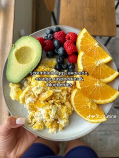 a person holding a plate full of food with oranges, raspberries and an avocado