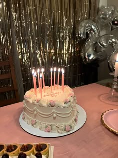 a birthday cake with lit candles sitting on top of a table next to other desserts