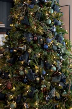 a christmas tree with ornaments and lights in the corner is decorated with plaid, green and blue