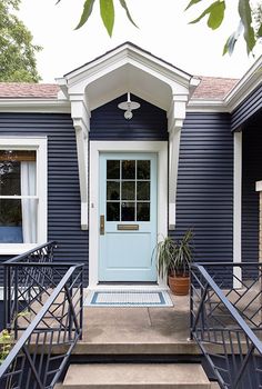 a blue house with stairs leading to the front door and potted plants on either side