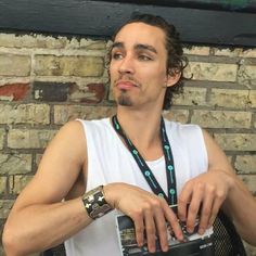 a man holding a camera in front of a brick wall with a watch on his neck