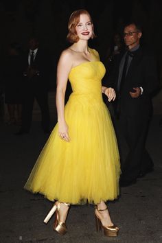 a woman in a yellow dress and gold shoes is walking with her hand on her hip