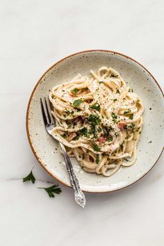 a white bowl filled with pasta covered in parmesan cheese and garnished with herbs