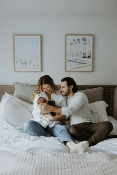 Mother and father happily sitting on a bed with their newborn son, looking down at him in the mother's arms and smiling.