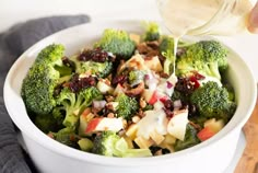 a person pouring dressing into a bowl of broccoli and cranberry salad