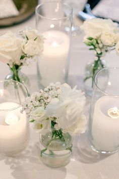 white flowers and candles sit in glass vases on a table