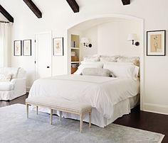 a white bed sitting in a bedroom next to two chairs and a rug on top of a hard wood floor