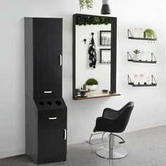 a black cabinet sitting next to a chair in a room with shelves and plants on the wall