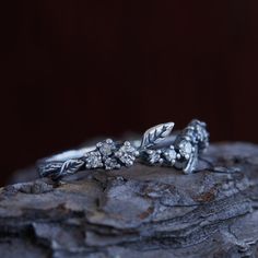 a silver ring with leaves and flowers on it sitting on top of a piece of wood