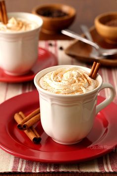 two mugs of hot chocolate with cinnamon sticks in them on a red saucer