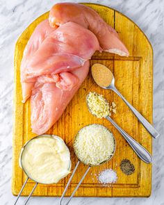 raw chicken on a cutting board with ingredients to make the sauce in small spoons