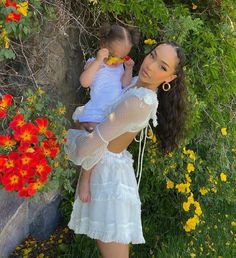 a woman is holding a baby in her arms and posing for the camera with flowers behind her