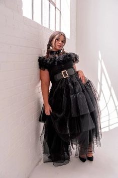 a woman in a black dress leaning against a wall