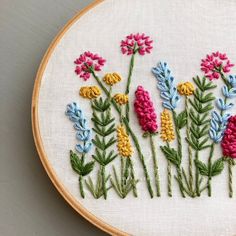 a close up of a embroidery on a hoop with flowers in the middle and one flower at the bottom