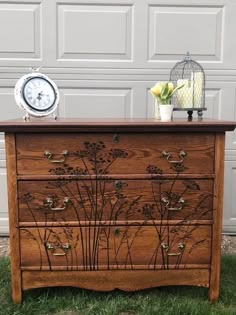 a wooden dresser with flowers painted on the front and sides, next to a birdcage