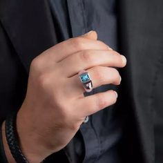 a man wearing a ring with a blue stone on it's middle finger and black shirt