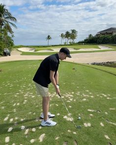 a man in black shirt and white shorts hitting a golf ball on green field with palm trees