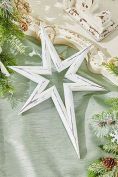 two white wooden stars sitting on top of a table next to evergreen branches and pine cones