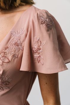 the back of a woman's pink dress with embroidered flowers on it and short sleeves