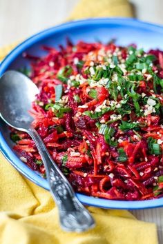 a blue bowl filled with shredded red cabbage and green onions next to a spoon on a yellow napkin