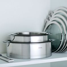 several stainless steel pots and pans on a white shelf next to a cell phone