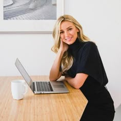 a woman sitting at a table with a laptop in front of her, smiling for the camera