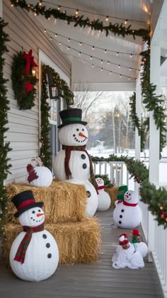 some snowmen sitting on hay bales in front of a house decorated for christmas