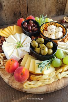 an assortment of cheeses, fruits and crackers on a wooden platter