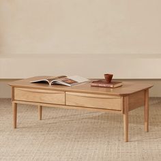 a coffee table with a book and cup on it in front of a beige wall