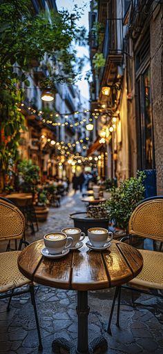 two cups of coffee sit on an outdoor table in the middle of a narrow alleyway