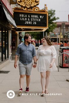 a man and woman walking down the street holding hands in front of a theater marquee