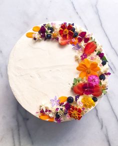 a cake with white frosting and colorful flowers on the top is sitting on a marble surface