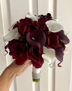 a bridal bouquet with red roses and white calla lilies is held by a woman's hand