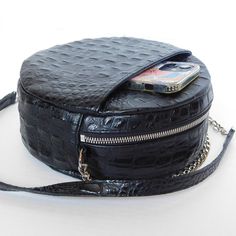 The always on-point classic black purse keeps you moving from work to play. The Classic Black Circle Purse’s updated design is a perfect blend of fashion and function with a front pocket for your cell phone and the addition of UCAN Luxury Zippers. Circle Cross-body purse Top Zipper - USA Front Cell Phone Pocket Inner Pouch Pocket Chain and Leather Strap Blue Berry Lining Black Leather - USA Approx: L 8” X H 8" X W 3" Strap: 48” Manufactured in Los Angeles, CA Black Phone Bag With Zipper Pocket Crossbody, Black Phone Bag For On-the-go, Black Bags With Removable Pouch Round Case, Black Bags With Removable Pouch And Round Case, Black Bag With Removable Pouch And Round Case, Black Bags With Removable Pouch In Round Case Shape, Chic Black Phone Bag With Cell Phone Pocket, Black Round Case Bag For Daily Use, Black Phone Bag With Cell Phone Pocket For On-the-go