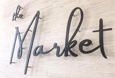 a sign that says market hanging on the side of a white wall with black lettering