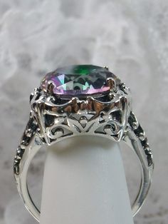 6 carat Simulated or Natural Rainbow Mystic Topaz Solid Sterling Silver RingSpeechless Design#D103 This filigree ring is a reproduction of a sterling silver Victorian antique with a stunning 6 carat Mystic Topaz gemstone solitaire. Please choose between simulated or natural gemstones. This full cut round faceted gem is 12mm in diameter. The inside of the band is marked 925 for solid sterling silver. Notice the beautiful bow and floral design of the silver filigree setting and band. This is a lo Vintage Iridescent Rings For Wedding, Iridescent Sterling Silver Rings For Formal Occasions, Iridescent Sterling Silver Wedding Jewelry, Victorian Sterling Silver Topaz Ring, Unique Silver Topaz Ring For Wedding, Silver Victorian Topaz Ring For Formal Occasions, Elegant Iridescent Topaz Gemstone Ring, Ornate Silver Topaz Ring For Gift, Elegant Iridescent Round Topaz Ring