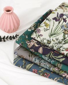 a pink vase sitting on top of a white table next to different types of fabrics