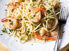 pasta with shrimp and parsley on a white plate next to a fork, knife and napkin