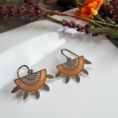 two pairs of earrings sitting on top of a table next to flowers and a vase