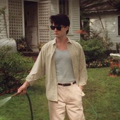 a man holding a hose in his hand while standing next to a lawn with a house behind him