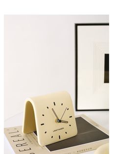 a white clock sitting on top of a table next to a framed photo and book