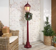 a red lamp post with a wreath on it next to a chair and potted plant